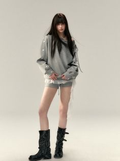 Woman with long dark hair wearing a gray sweatshirt, shorts, and black boots