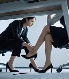 Two women in business attire under a desk, one touching the other's leg