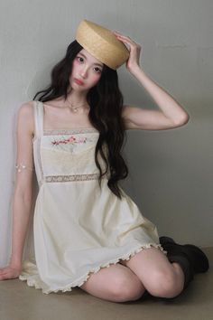 Woman with long dark hair wearing a straw hat and an embroidered dress, sitting indoors