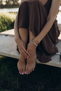 Woman in a brown dress with bare feet and a pearl bracelet outdoors