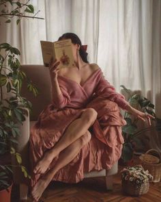 Woman in a pink dress reading a book indoors with plants