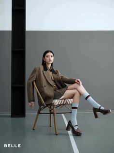 Woman in a plaid blazer and short skirt sitting on a chair indoors