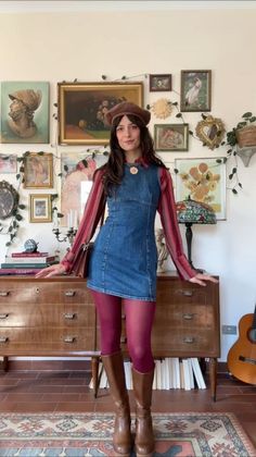 Woman in a denim dress, red tights, and beret standing in a room with framed art