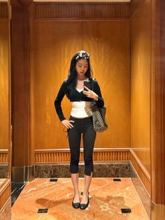 Woman in a black cropped cardigan and capri leggings taking a mirror selfie