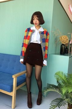 Woman with short hair wearing a colorful cardigan and brown skirt indoors