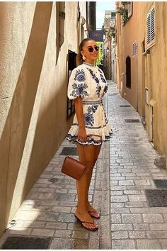 Woman in an embroidered dress and sunglasses standing on a narrow cobblestone street