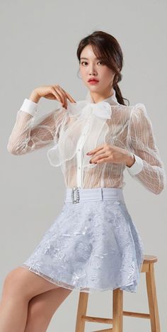 Woman in a sheer white blouse and light blue skirt posing in a studio