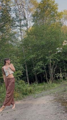 Woman in a crochet top and brown pants standing barefoot in a forest