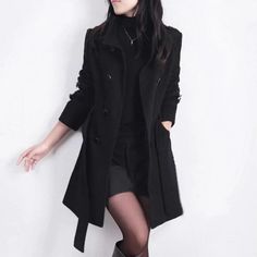 Woman in a black coat, turtleneck, shorts, and tights against a white wall