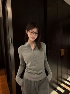 Woman with long hair and glasses wearing a gray shirt and sweatpants indoors