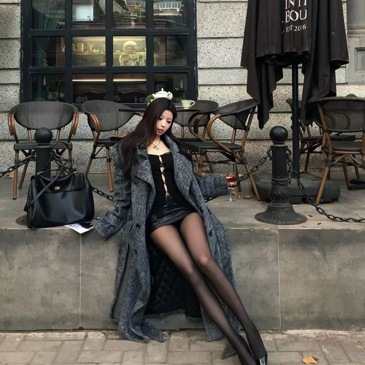 Woman in a long coat and mini skirt sitting outside a cafe