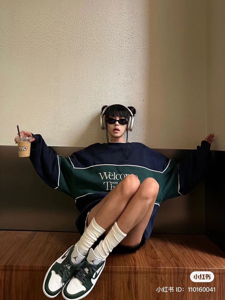 Person in an oversized sweatshirt, sunglasses, and headphones sitting indoors