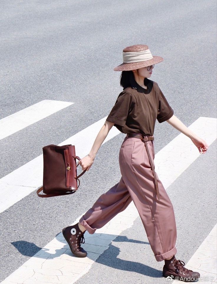 Person in a straw hat and wide-leg pants crossing a street