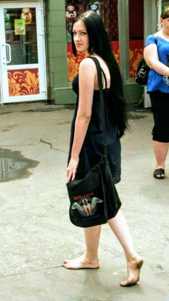 Woman with long black hair in a black dress walking barefoot on a street