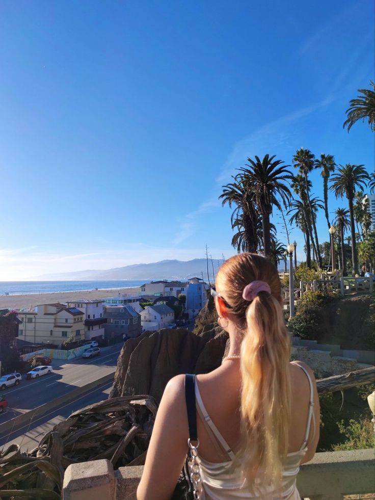 Woman with a ponytail looking out at a beach and cityscape with palm trees