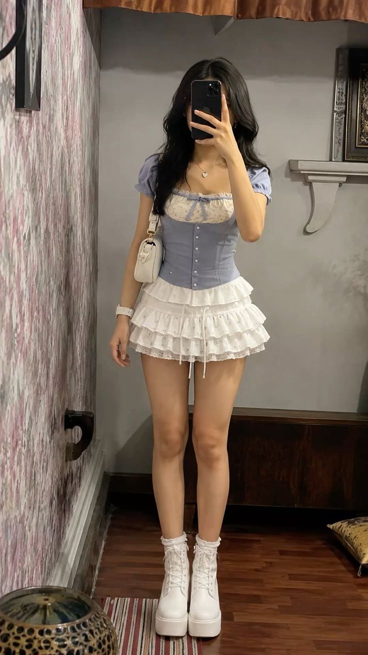 Woman in a blue corset top and white ruffle skirt taking a mirror selfie