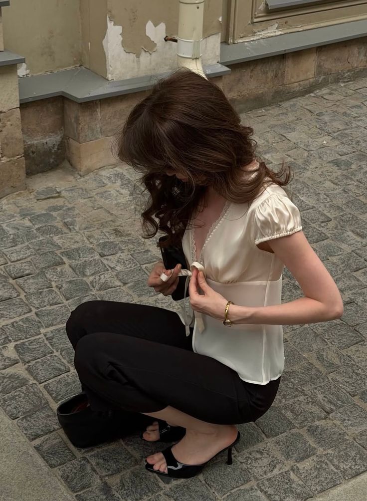 Woman with long wavy hair crouching on a cobblestone street