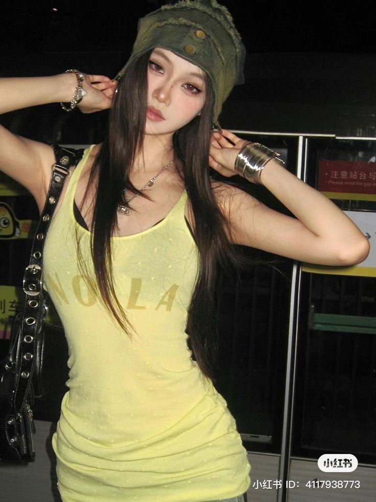 Woman with long dark hair and a green beanie wearing a yellow tank top
