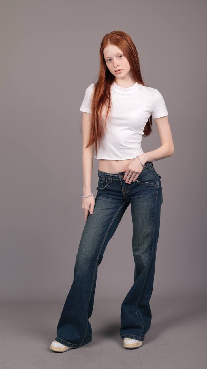 Young woman with long red hair wearing a white crop top and blue jeans