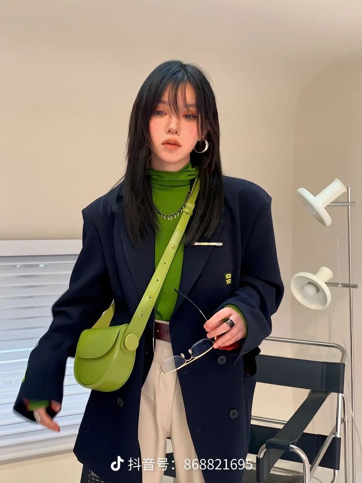 Woman with long black hair wearing a green turtleneck and black blazer indoors