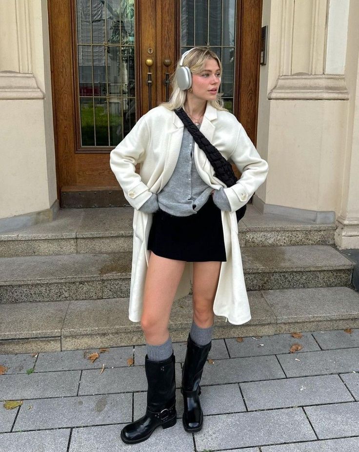 Blonde woman in a white coat, black mini skirt, and boots with headphones outdoors