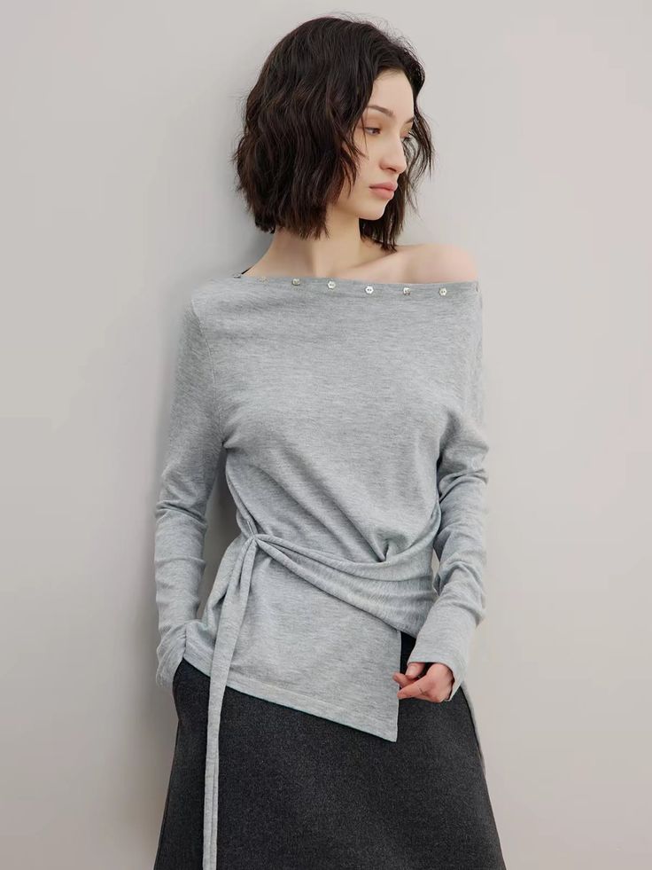 Woman with short hair wearing a grey off-shoulder top and dark skirt