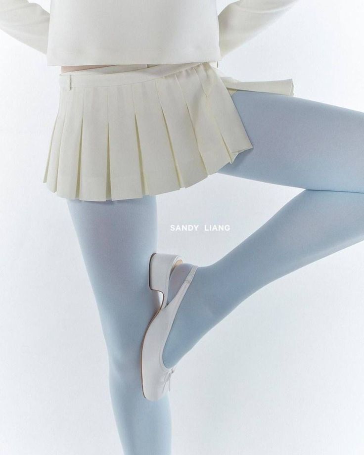 Person wearing a pleated skirt, blue tights, and white shoes in a studio