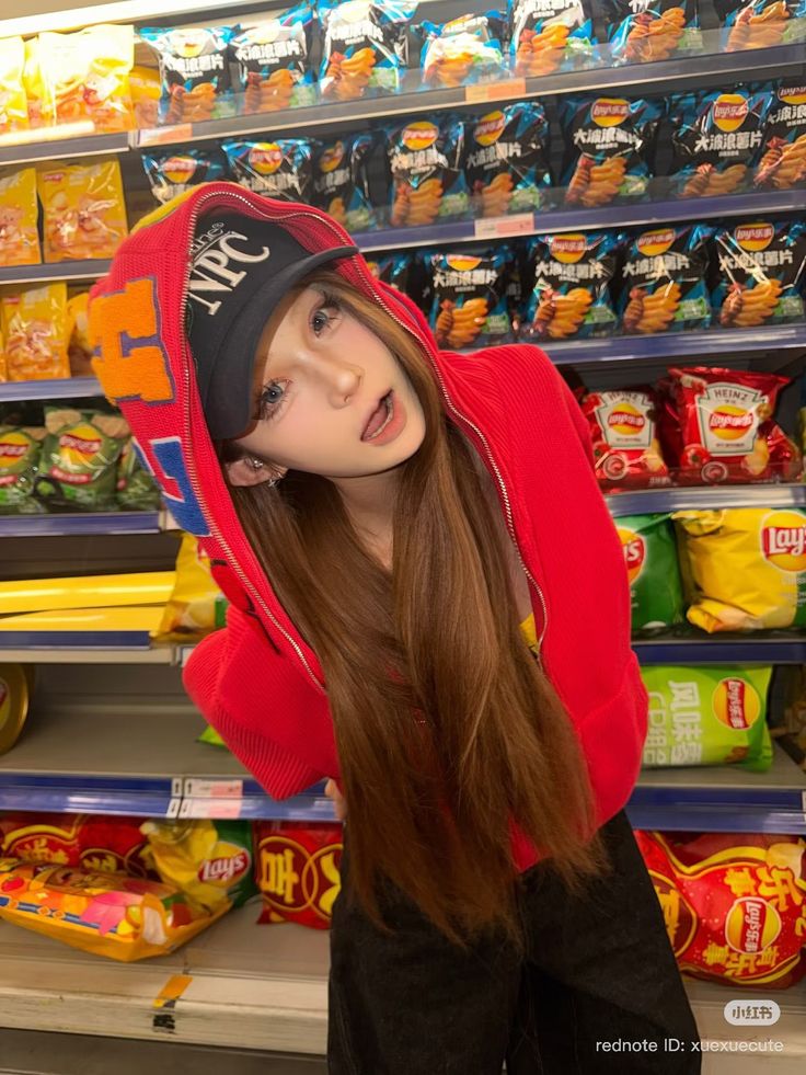 Person with long hair wearing a red hoodie and baseball cap in a supermarket aisle