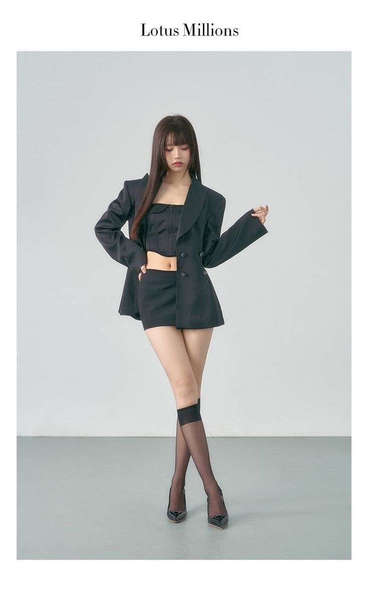 Woman in a black blazer, crop top, and mini skirt posing in a studio