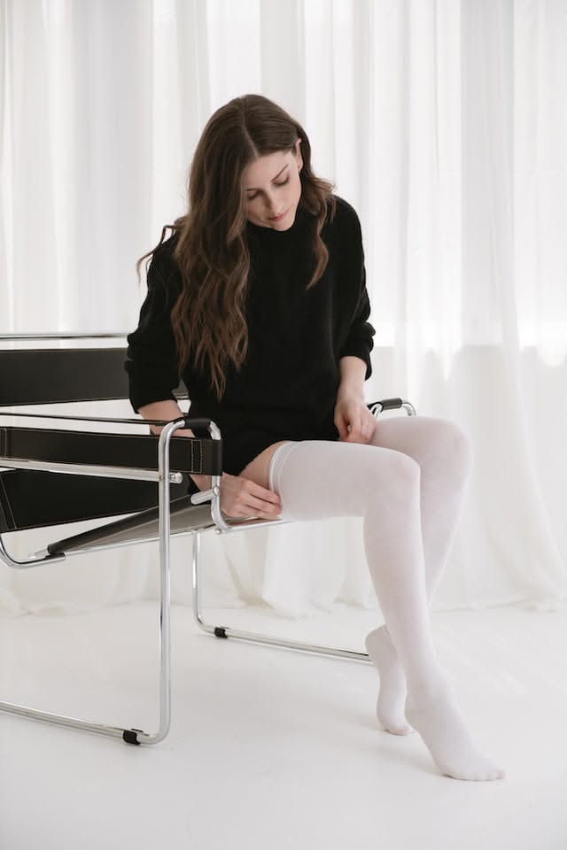 Woman in a black sweater and white thigh highs sitting on a chair