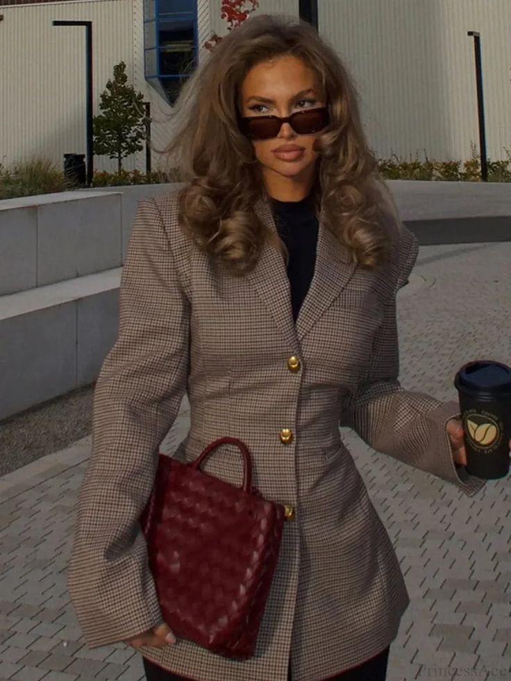 Woman with long wavy hair and sunglasses holding a red handbag and coffee cup