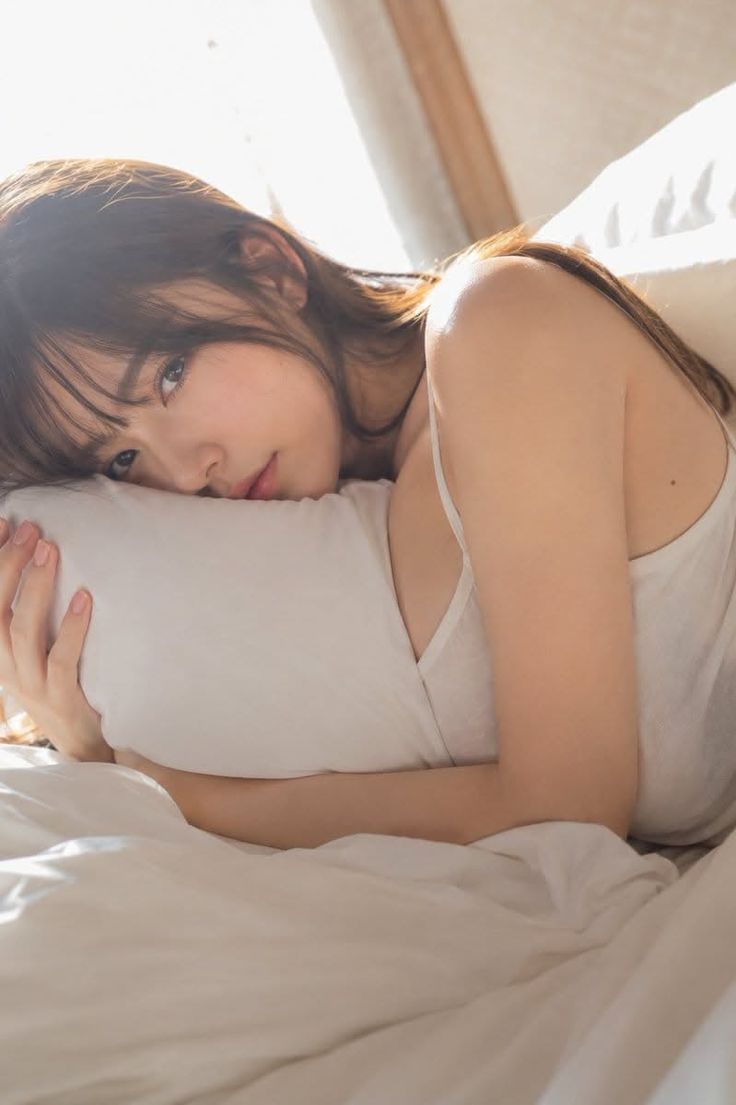 Woman with long hair in a white tank top lying on a bed