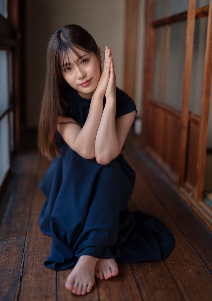 Woman with long hair in a dark dress sitting on a wooden floor indoors