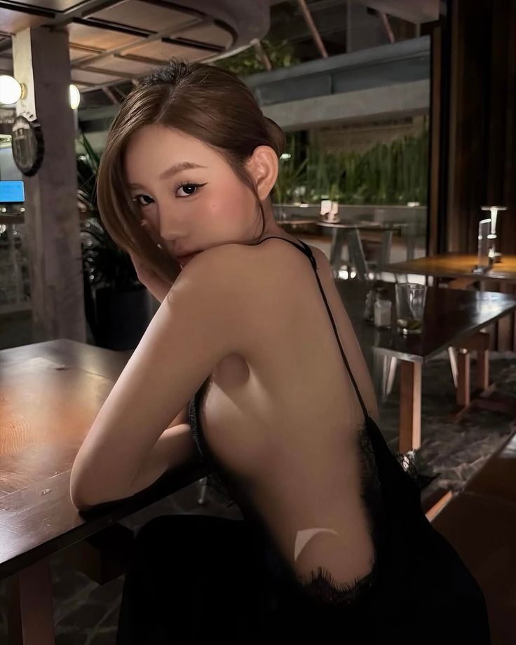 Woman in a black lace-trim dress posing suggestively indoors