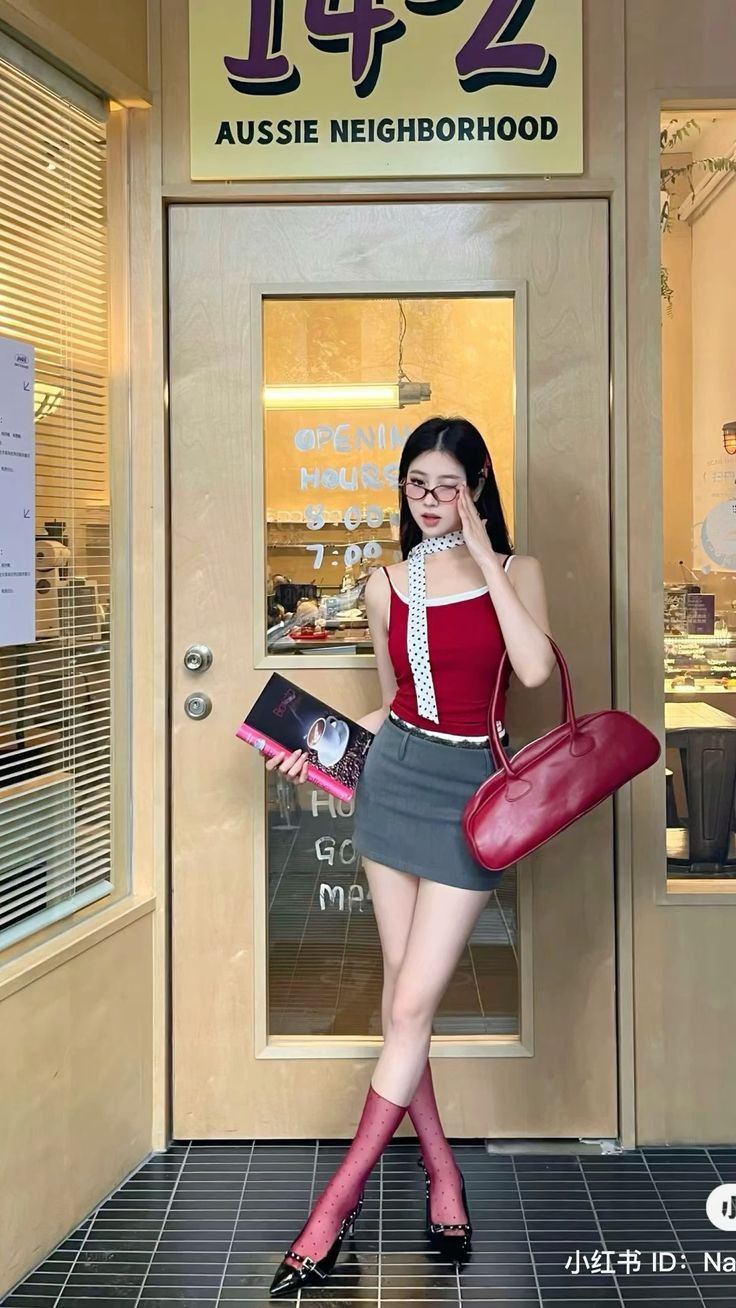 Woman in a red tank top and mini skirt holding a book and handbag