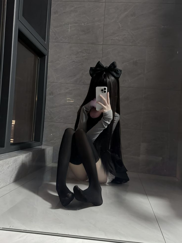 Person with long black hair and a bow taking a mirror selfie indoors