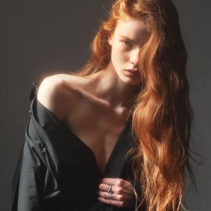 Woman with long red hair wearing an open black shirt with exposed skin
