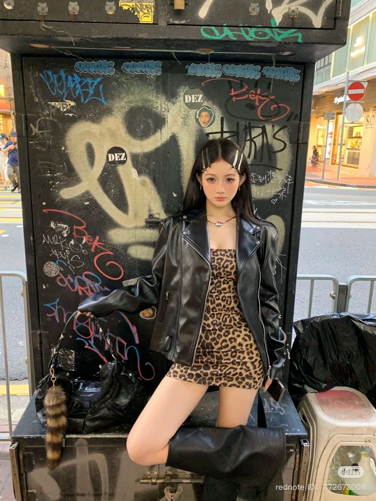 Woman in a leopard print dress and leather jacket posing against a graffiti-covered wall