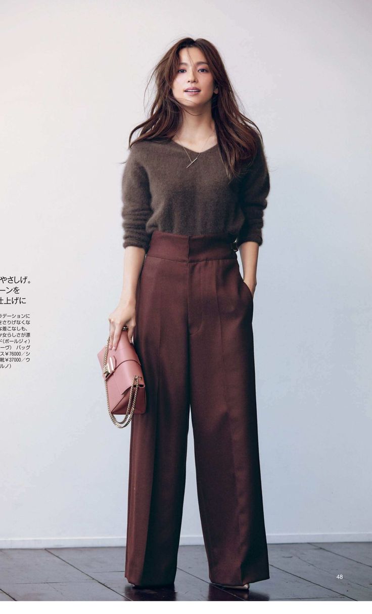 Woman with long hair wearing a brown sweater and wide-leg pants, holding a pink handbag