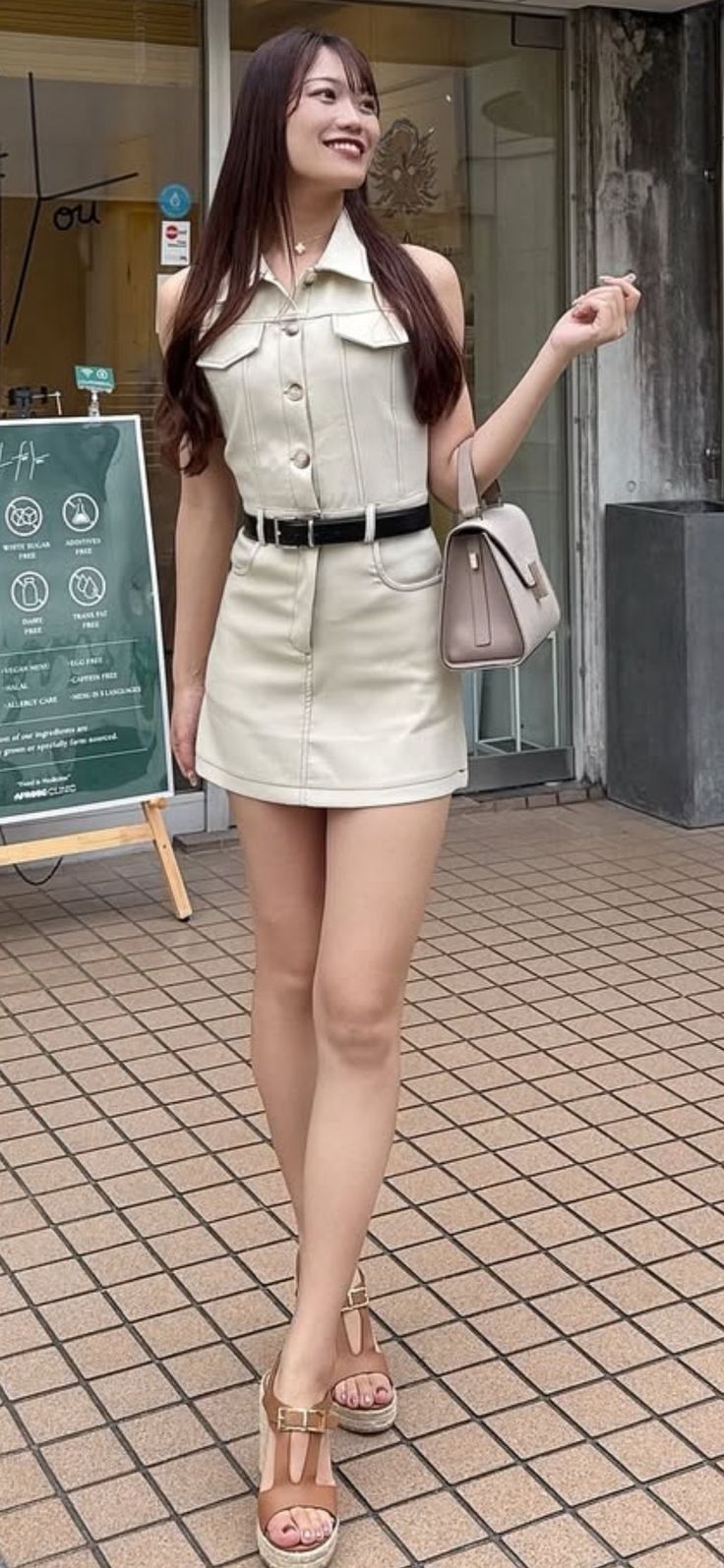 Woman in a light-colored sleeveless top and mini skirt with a handbag outdoors