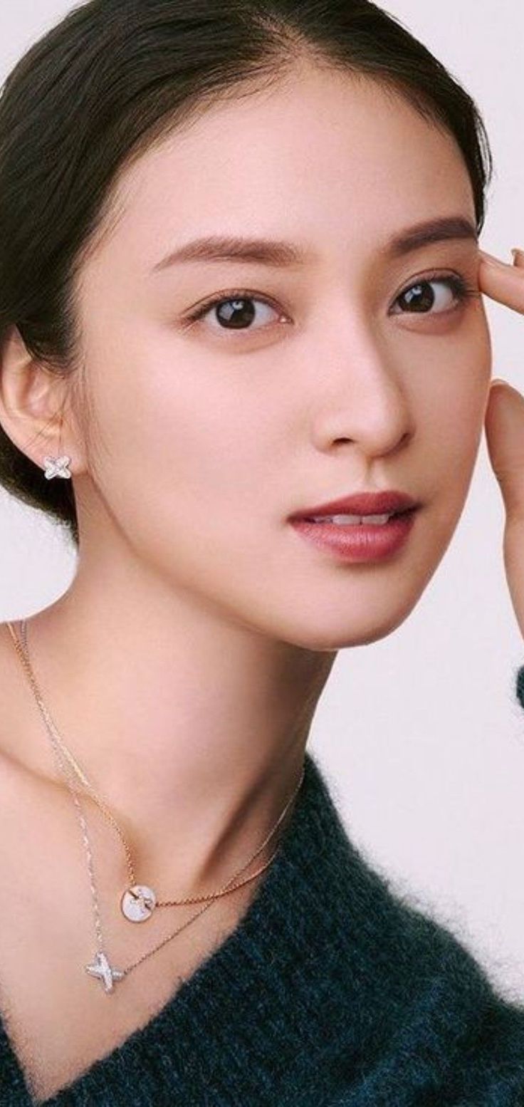 Woman with dark hair wearing earrings and a necklace with a green sweater