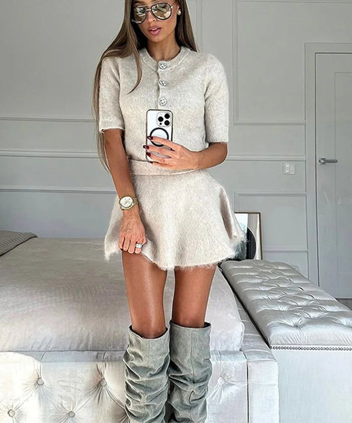 Woman in a beige knit set and knee-high boots taking a mirror selfie