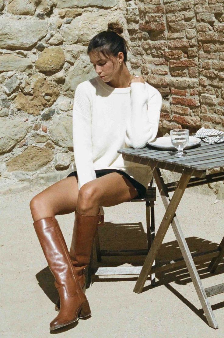 Woman in a white sweater and brown boots sitting at a wooden table outdoors