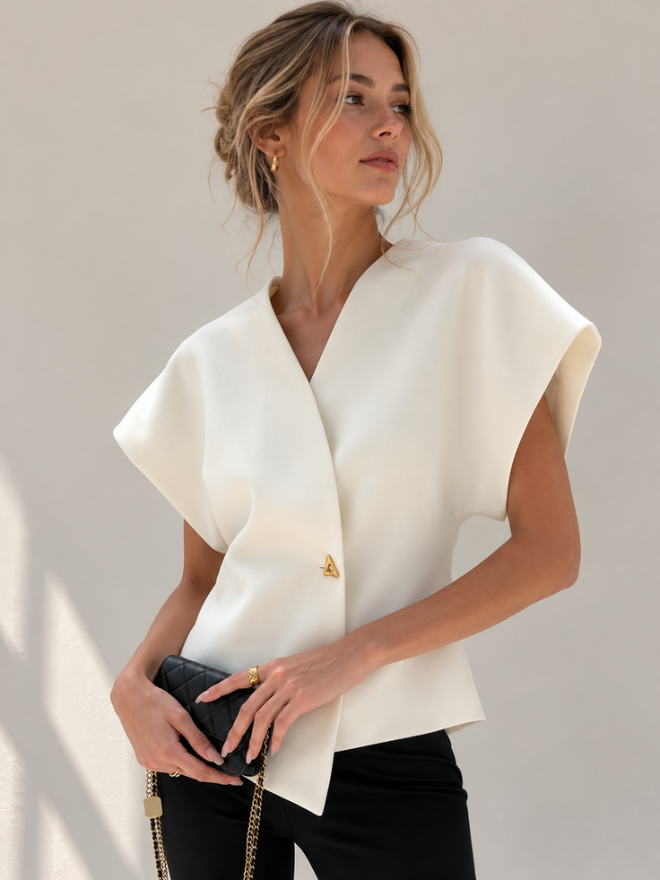 Woman with blonde hair in an updo wearing a white top and black pants, holding a quilted bag
