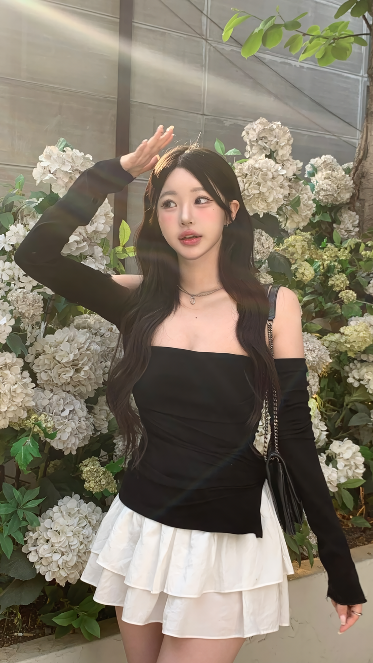 Woman with long dark hair in a black top and white skirt outdoors with flowers