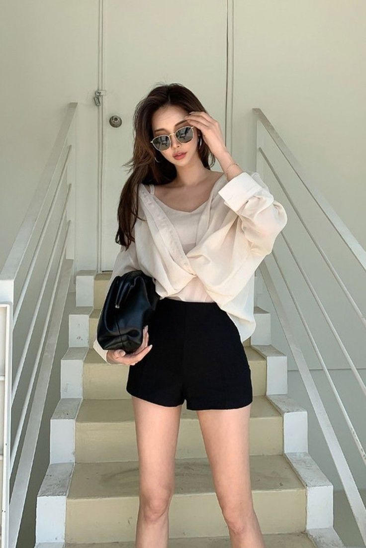 Woman in sunglasses, white shirt, and black shorts holding a handbag on stairs