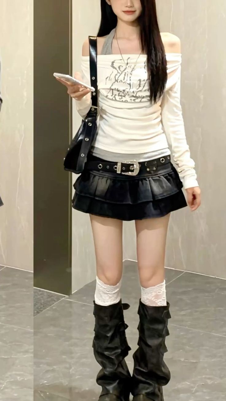 Woman in an off-shoulder top, mini skirt, and black boots holding a phone