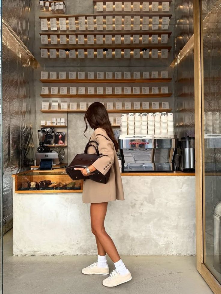 Woman in a blazer dress and sneakers holding a handbag in a modern cafe