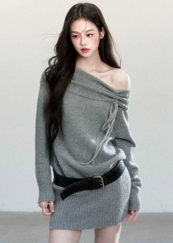 Woman with long dark hair wearing an off-shoulder gray sweater and black belt