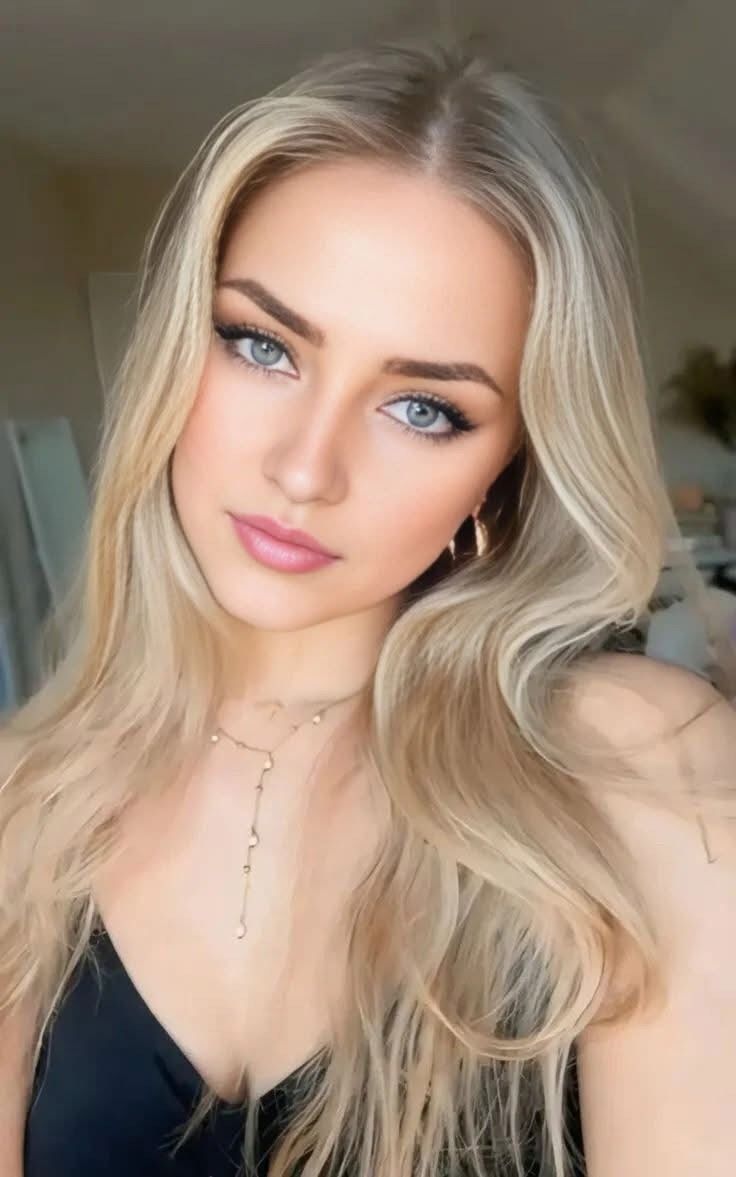 Blonde woman with blue eyes and long hair wearing a necklace and earrings